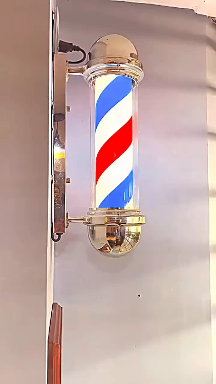 Poste de barbero rojo, blanco y azul encendido en el muro
